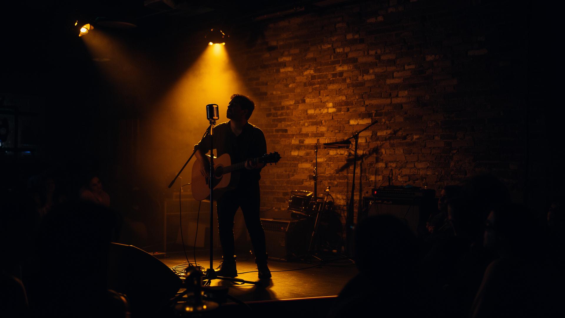 Singer-songwriter under warm stage light at an intimate venue